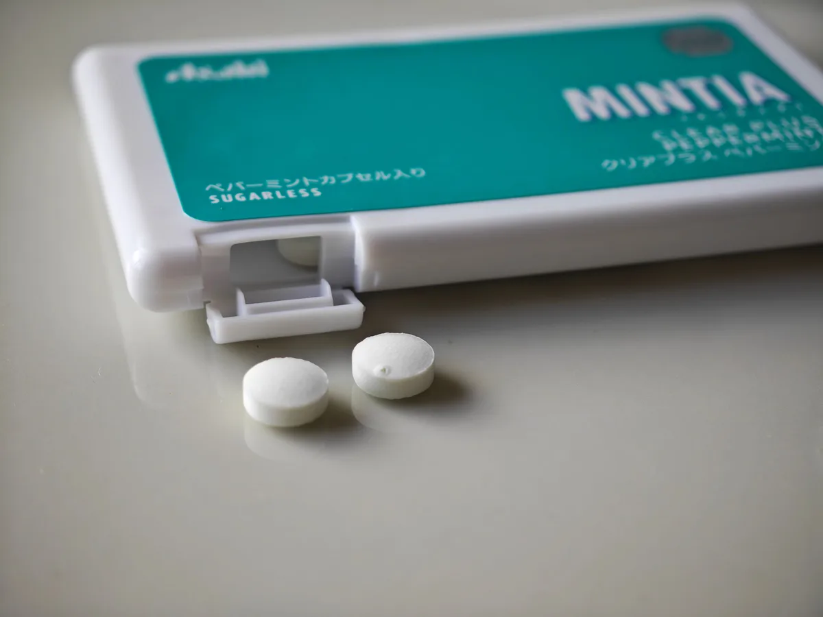 Two MINTIA Clear Plus Peppermint tablets beside the mint green case