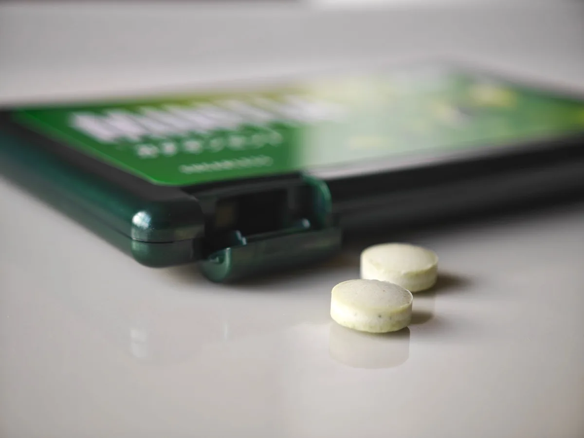 Two MINTIA Catechin Mint tablets beside the green case