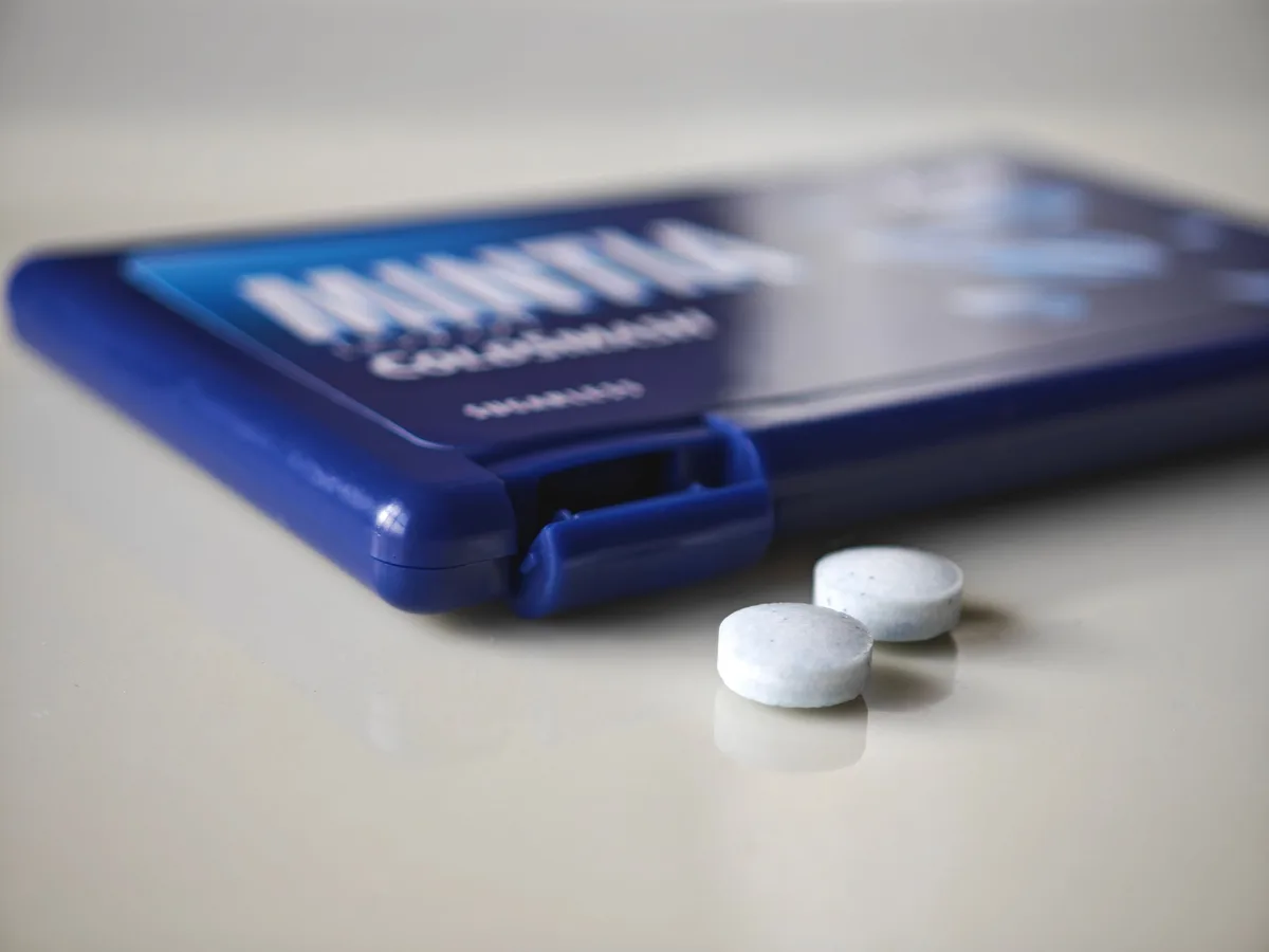 Two MINTIA Cold Smash tablets beside the dark blue case