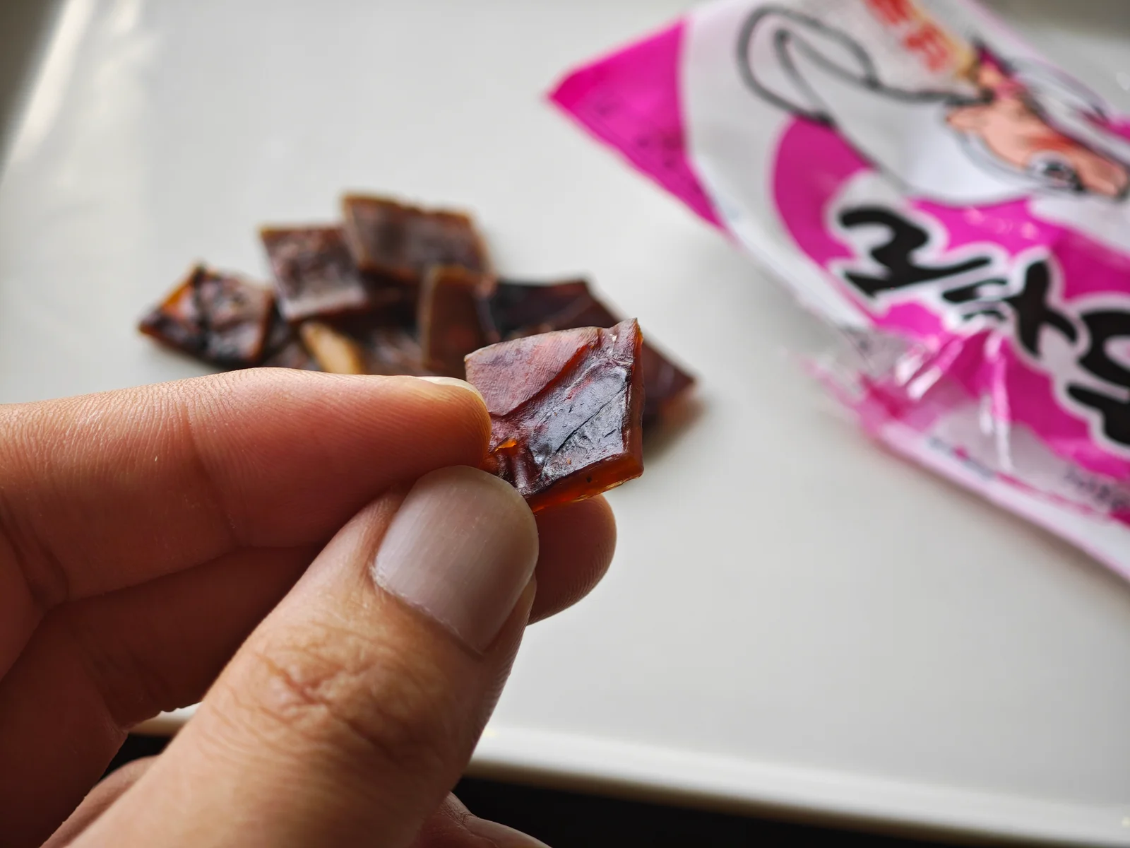 Hand holding one sweet-spicy Cut Yocchan piece to show its net-grill-like sheet shape