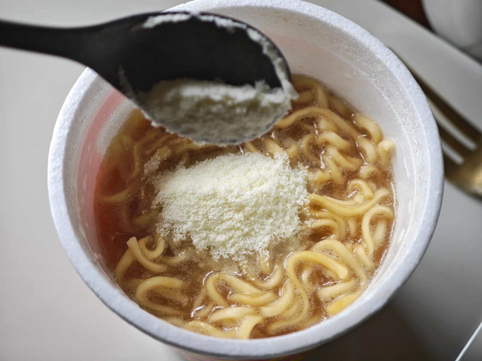 A spoonful of milk powder being added to tonkotsu Butamen