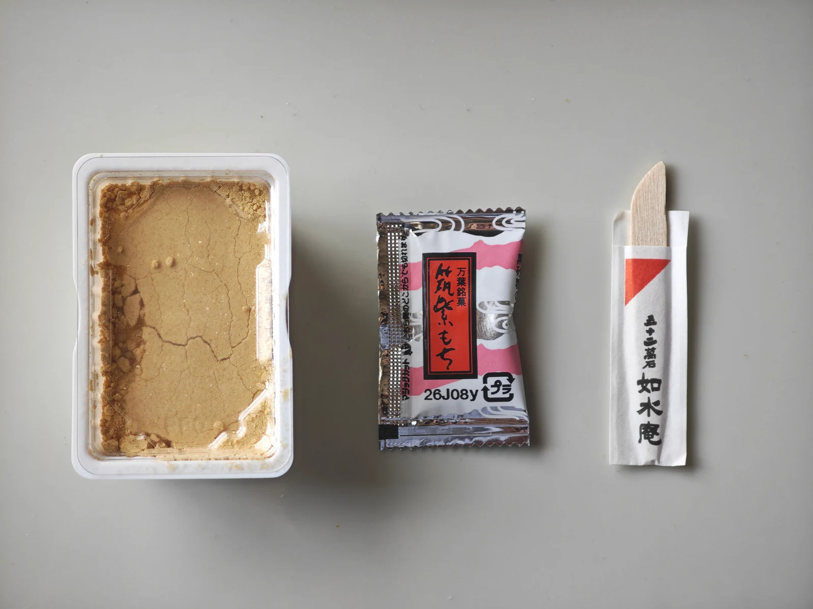Tsukushi Mochi tray, kuromitsu packet, and wooden pick arranged from left to right