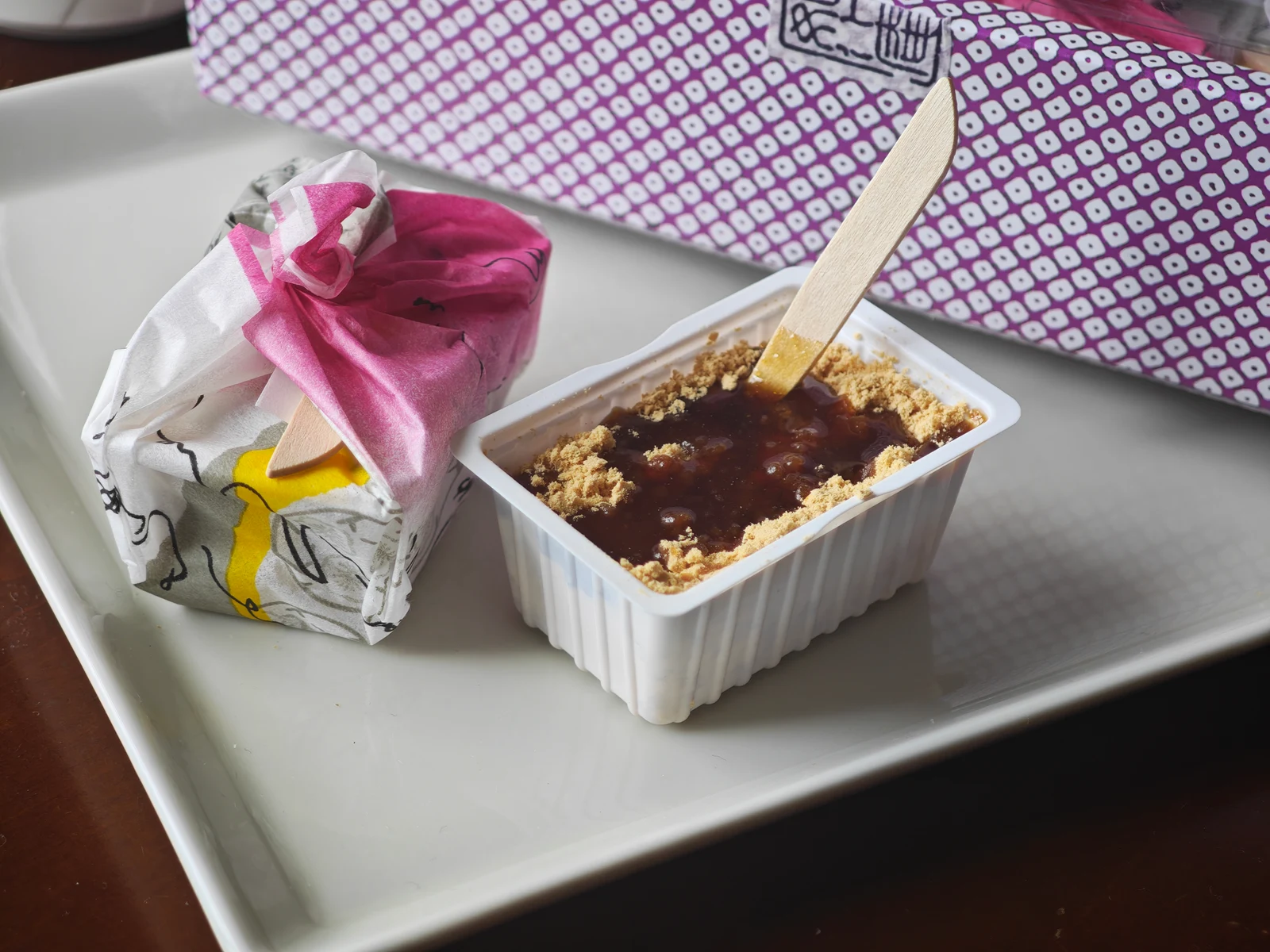 Prepared Tsukushi Mochi with kuromitsu beside its individual wrapper and purple gift box