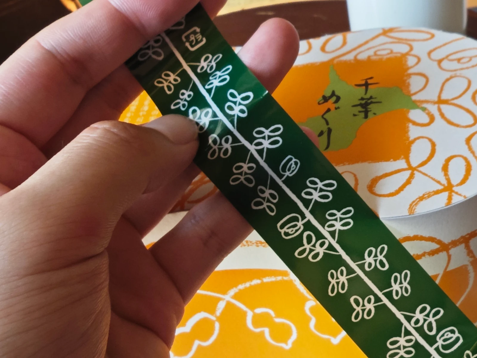 Hand holding the green printed band that wraps the Chiba Meguri box