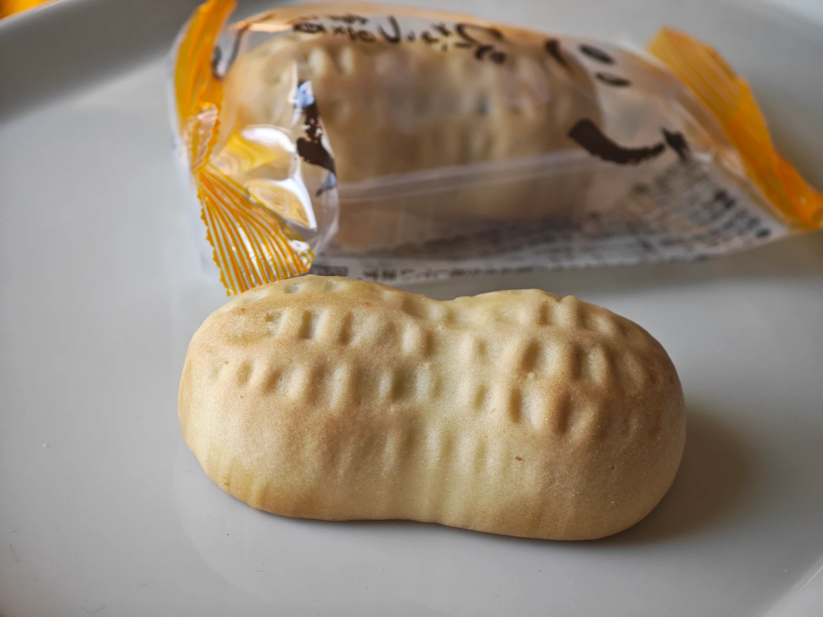 Unwrapped Peanut Manju with peanut-shell ridges beside its yellow-patterned package